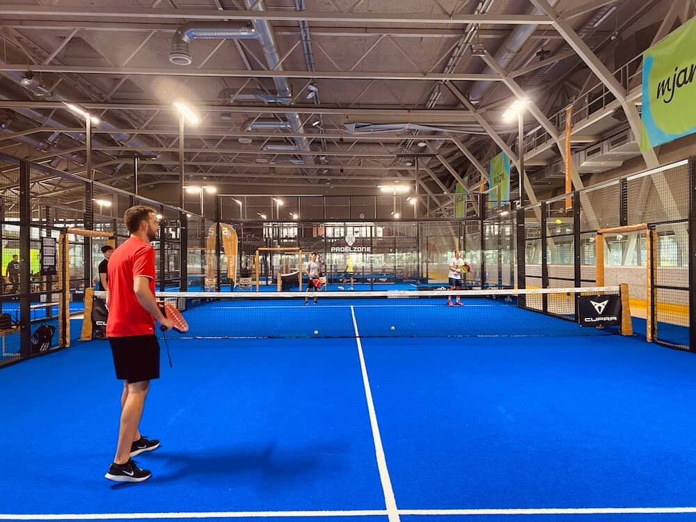 Padel Tennis Feld von der Rückseite der Glaswand fotografiert. Zu sehen sind 3 Spieler.