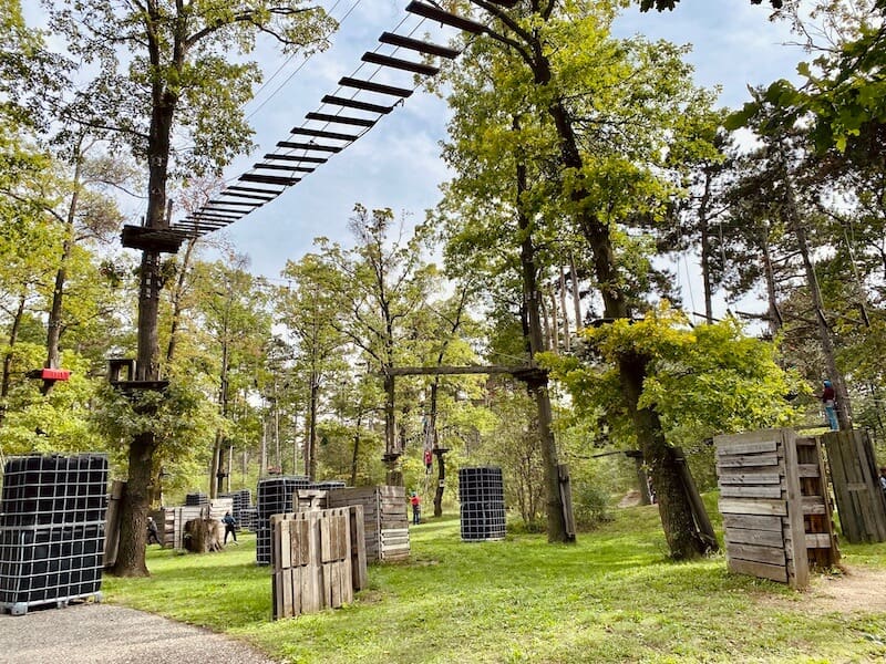 Nerftag und Lasertag Areal im Erlebnispark Gänserndorf. Bäume mit Leitern und untern Wiese mit aufgestellten Holzbunkern für die Nerftagspieler.