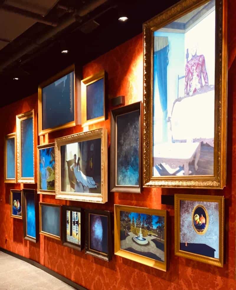 Gallerie in Mythos Mozart. Digitale Bilderrahmen hängen an einer rot tapezierten Wand.