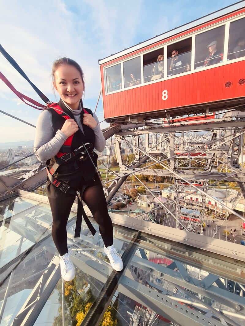 Mädchen steht auf der Glasplattform 9. Hinter ihr eine rote Garnitur des Riesenrads.