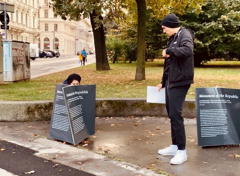 Frau hockt am Boden um auf einer Tafe Hinweise für die Schnitzeljagd zu finden. Daneben ein Herr, der zusieht.