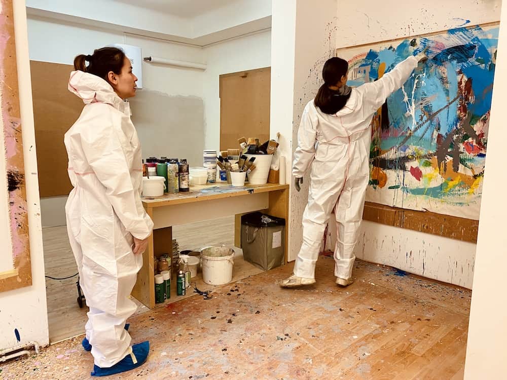Action Painting. Zwei Frauen im weißen Schutzanzug und einem Gemälde rechts zum üben von Akrylmalerei.