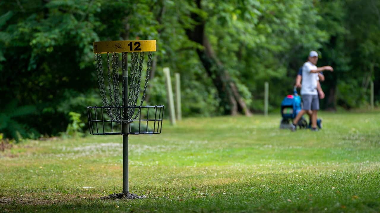 outdoor-aktivität: disc-Golf. Metallkorb umgeben von saftig grüner wieser. im hintergrund verschwommen ein spieler, der disc-golf spielt.