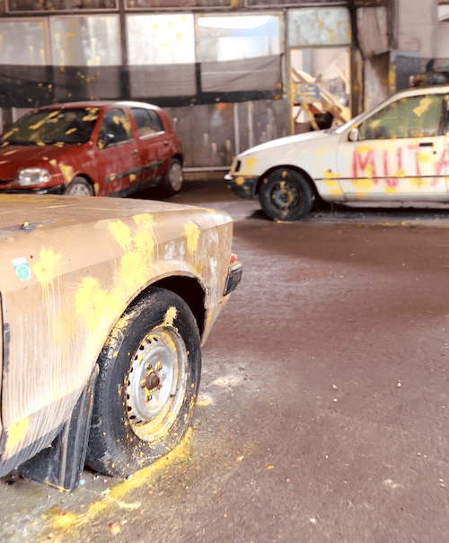 Autos voller Paintball Farben in einer Art Lagerhalle als Spielplatz.