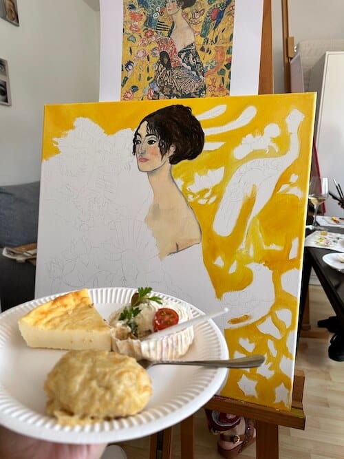 Halb fertig gemaltes Lady with fan von Gustav Klimt und Snacks auf einem Teller davor. BIld ist unfertig, dahinter die Vorlage für das Art Event.