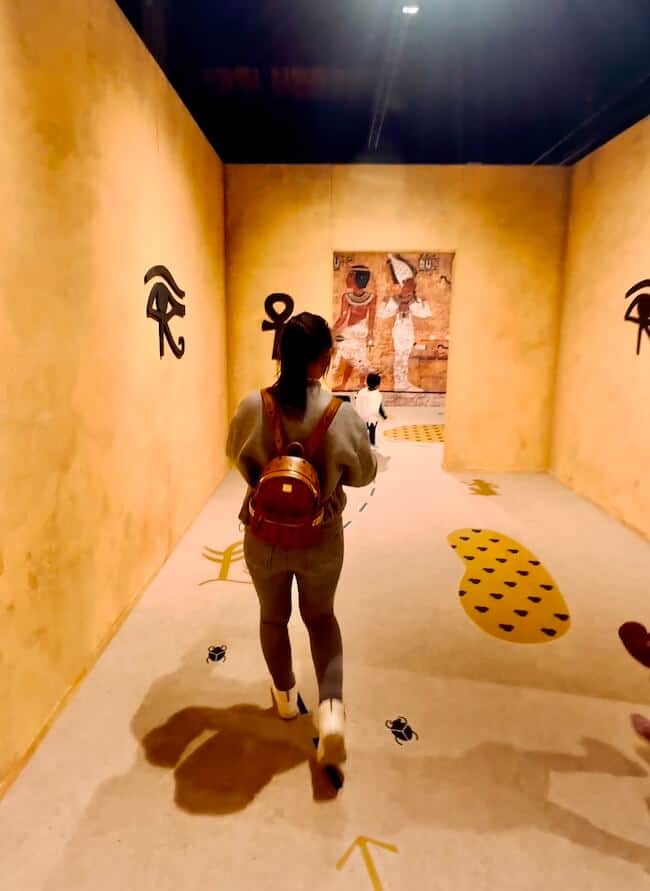 Frau mit Tablett in der Hand durchgeht kleinere Räume mit gelber Wandfarbe. Augmented Reality lässt den Raum zum leben erwecken.