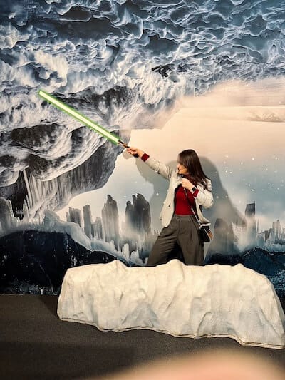 Frau hält Laser Schwert in der Hand und steht vor einer Foto-Kulisse: Schnee und Eisberge.