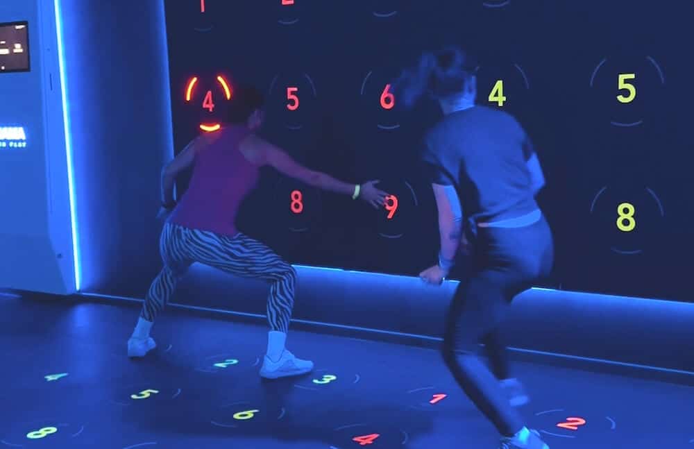 blauer Raum mit interaktiver Trainingswand und zwei Damen, davor stehen und in Bewegung sind