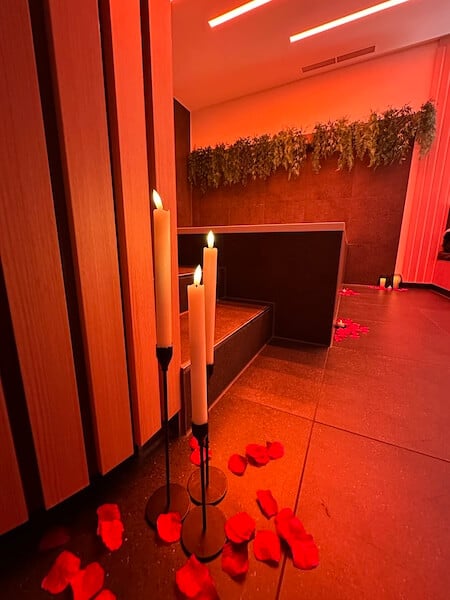 eine klassische private wellnesskabine. Kerzen und Rosenblüten stehen am Boden. Rotes Ambientelicht erfüllt den Raum