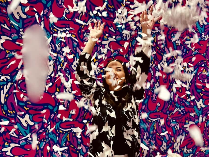 Pinker hintergrund und weiße Schnippsel fliegen umher. Frau hat dabei Spaß.