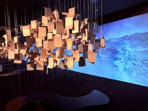 Installation in der Mitte des Raumes: Hängen Briefe an Fäden von der Decke hinunter. Blauer Hintergrund.