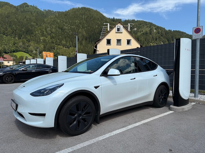 Weißes Tesla Y Auto beim Aufladen einer Supercharging Station am Land